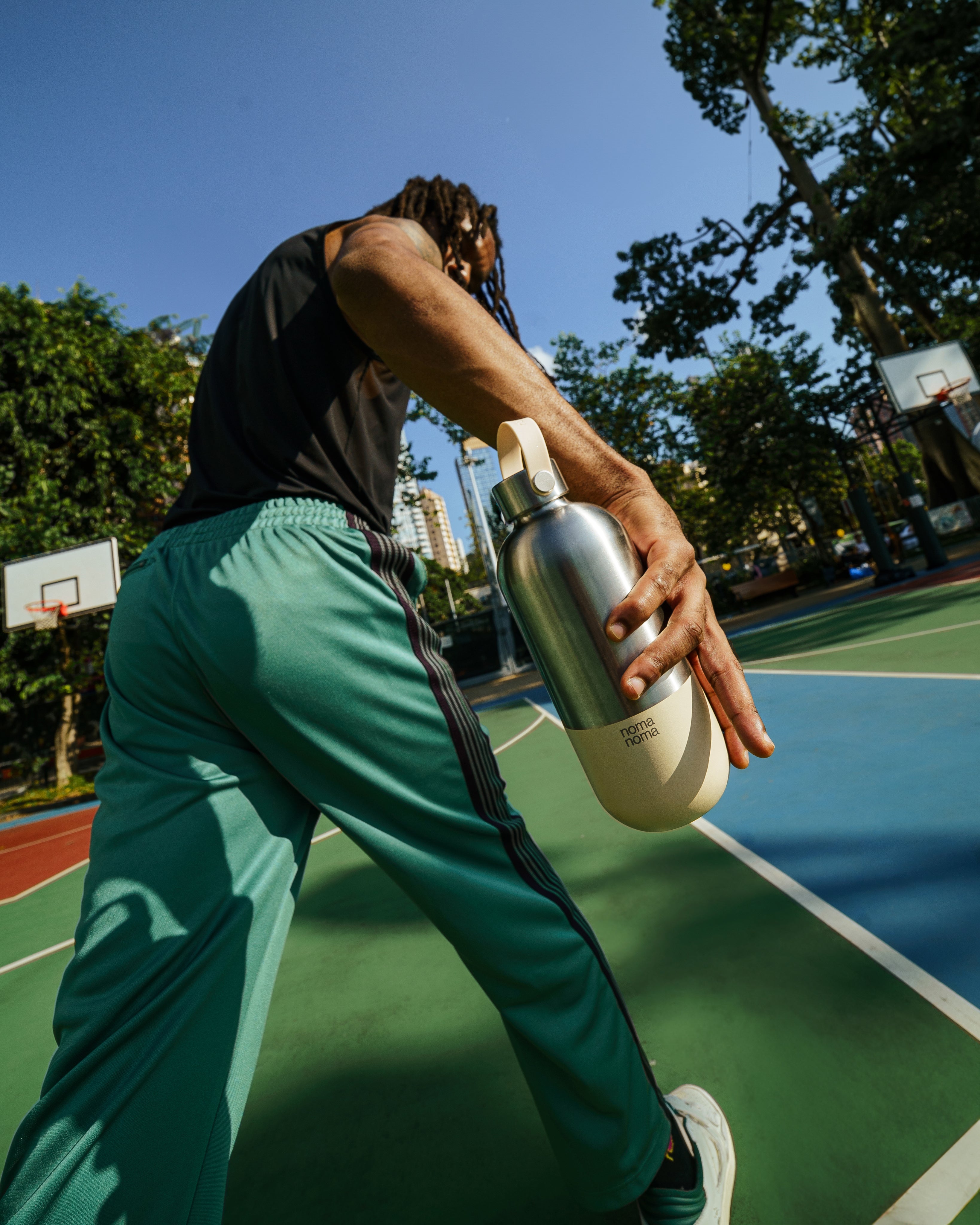 Kris spielt eine Runde Basketball in Hong Kong mit der beigen Thermosflasche von noma noma in der Hand