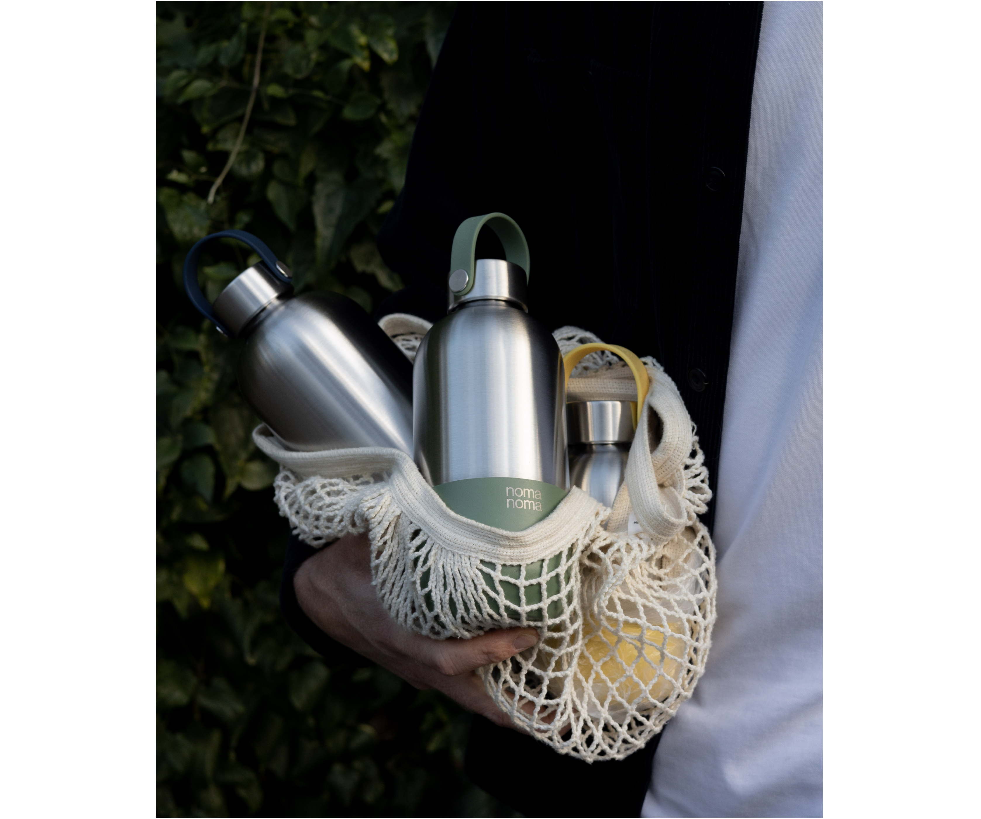 Drei noma noma Isolierflaschen liegen in einem Jutebeutel und werden von einem jemanden im Arm getragen.