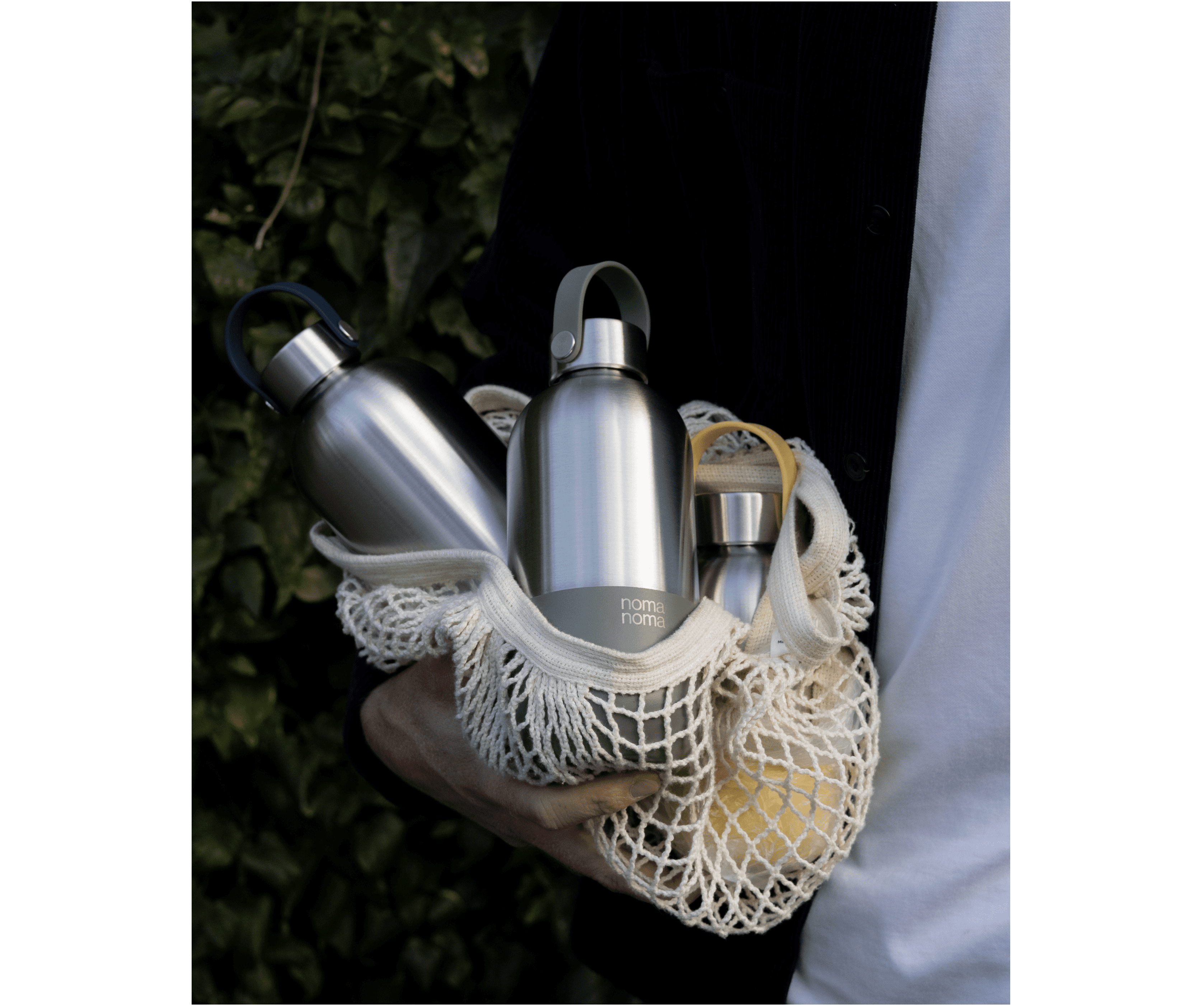 Drei noma noma Isolierflaschen liegen in einem Jutebeutel und werden von einem jemanden im Arm getragen.