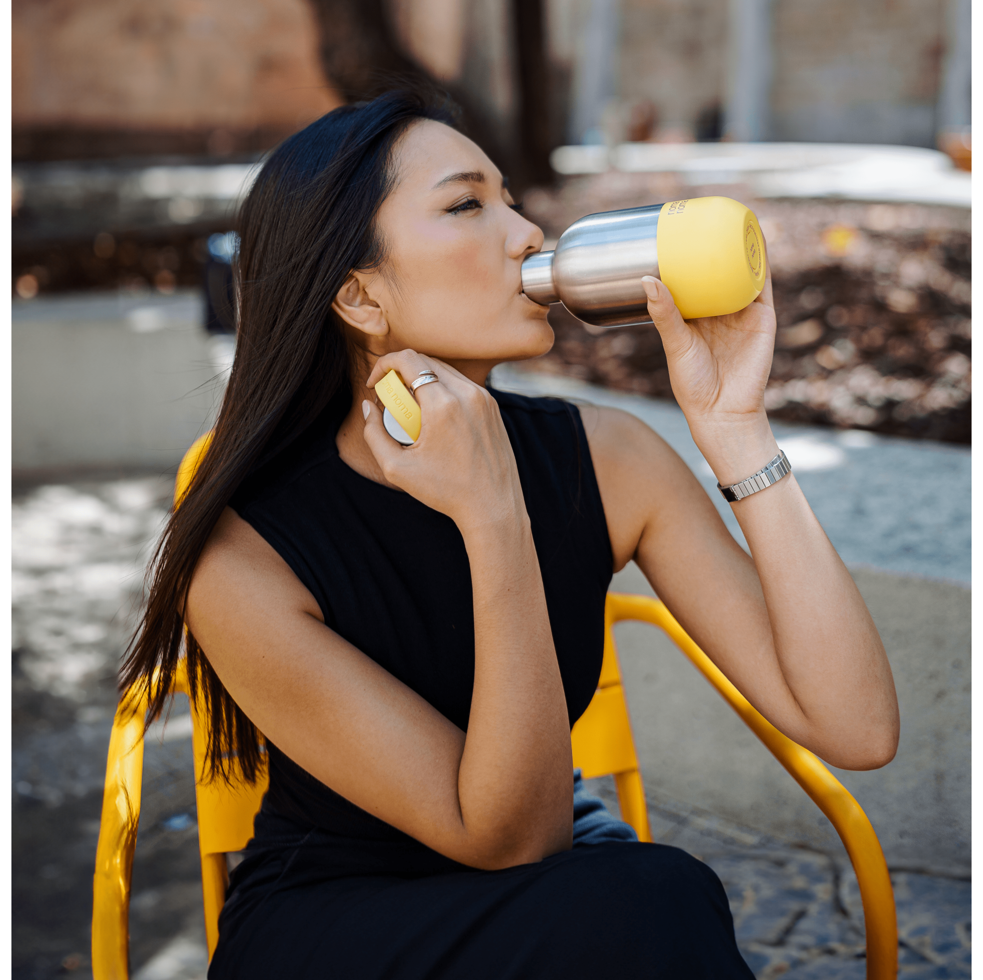 Eine sitzende Frau trinkt aus der 500 ml noma noma Isolierwasserflasche. 