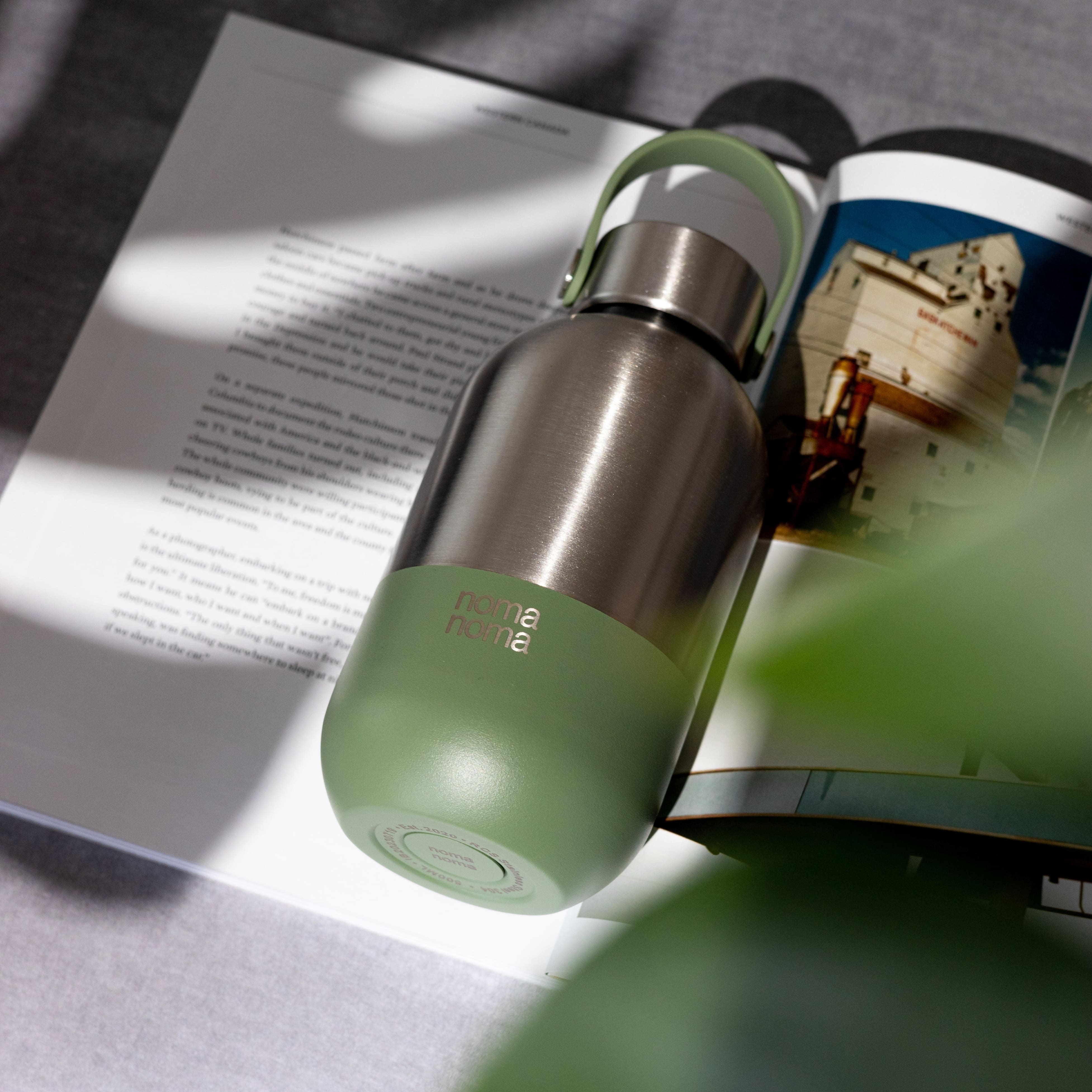 Die noma noma Edelstahl Wasserflasche in grün (500ml) liegt auf einem aufgefaltetem Buch