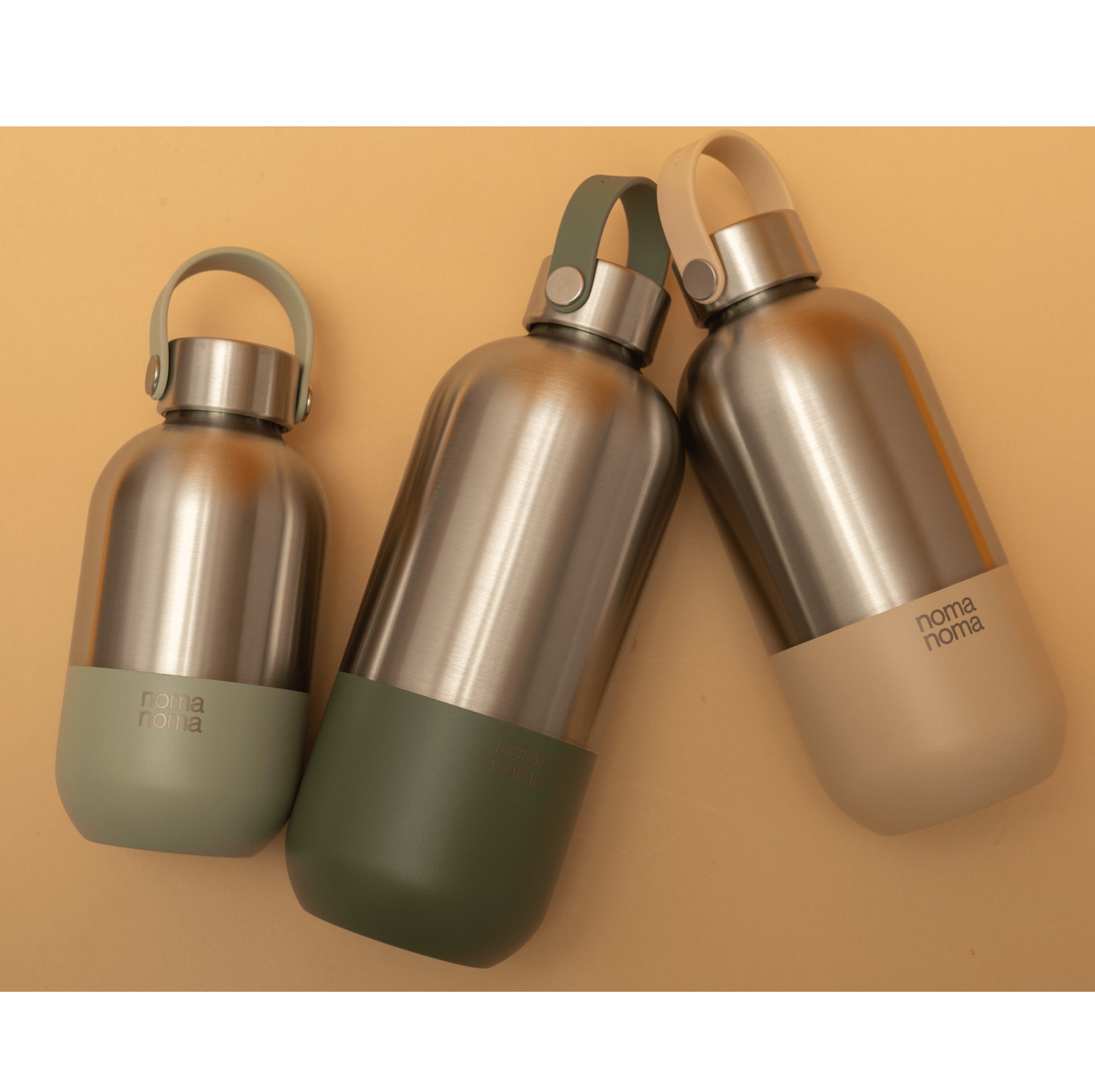 Drei noma noma Isolierflaschen in den drei verschiedenen Größen liegen auf einem hellen Hintergrund.